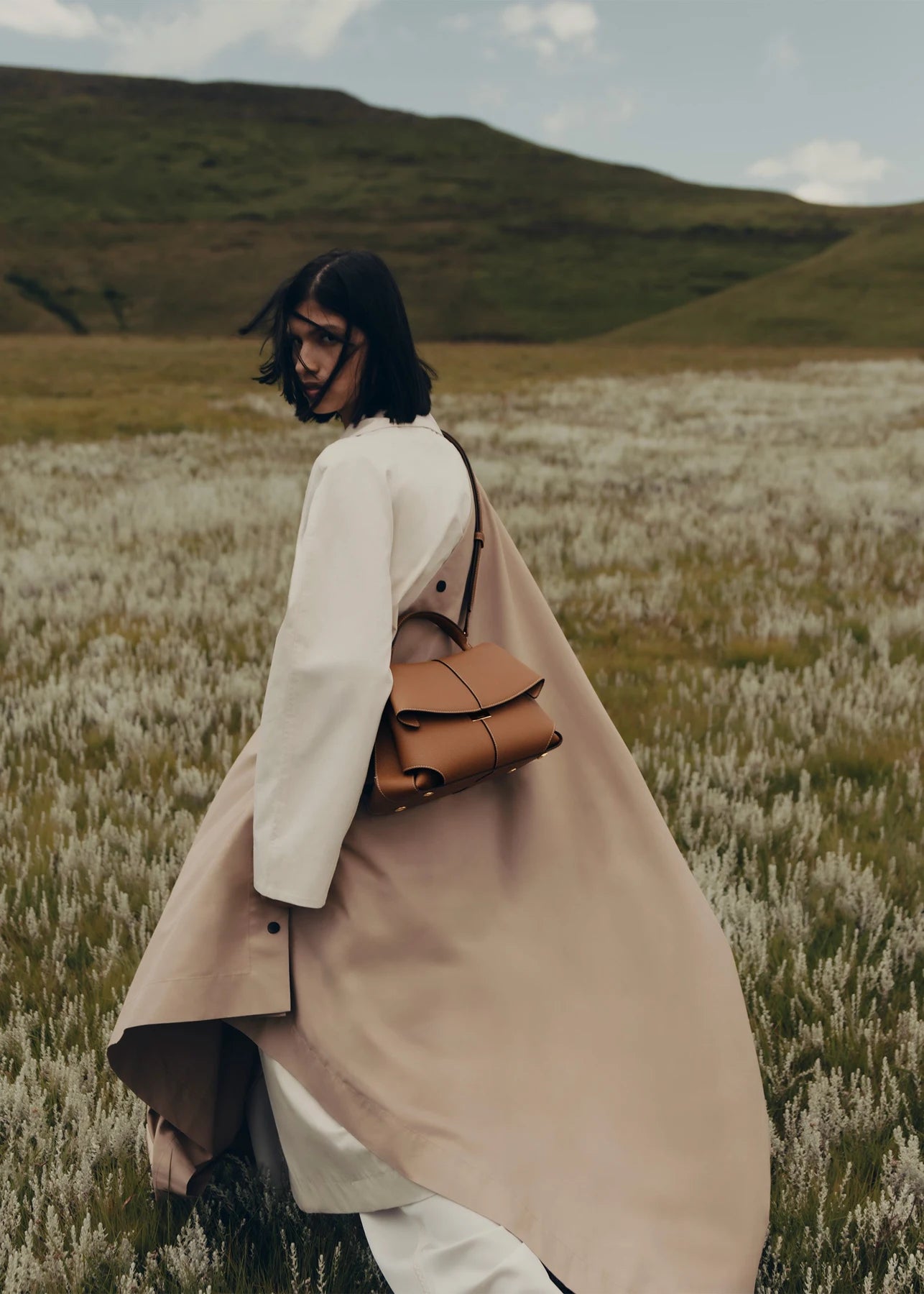 A camel handbag styled with a neutral outfit in a meadow